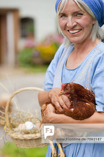 Reife Frau mit Korb mit frischen Eiern und Huhn