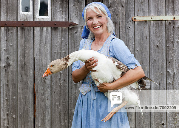 Mature woman with goose on farm