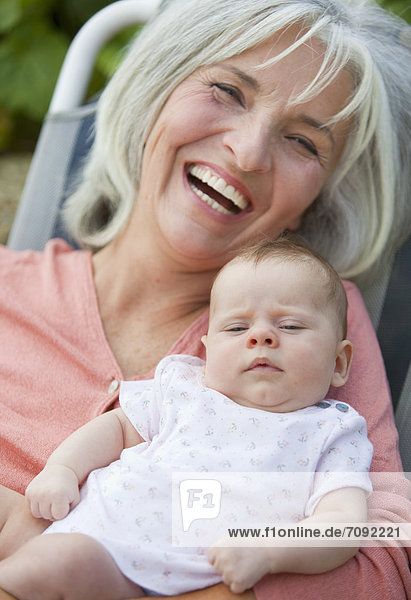 Frau mit Enkelkind im Gartenstuhl sitzend  lächelnd