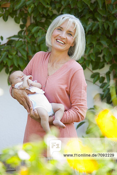 Frau mit Enkelkind in ihrem Garten  lächelnd