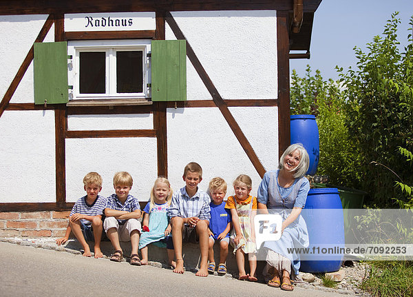 Woman sitting with group of children in front of small house