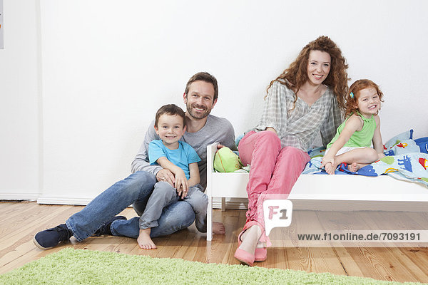 Germany  Berlin  Family sitting on bed  smiling  portrait