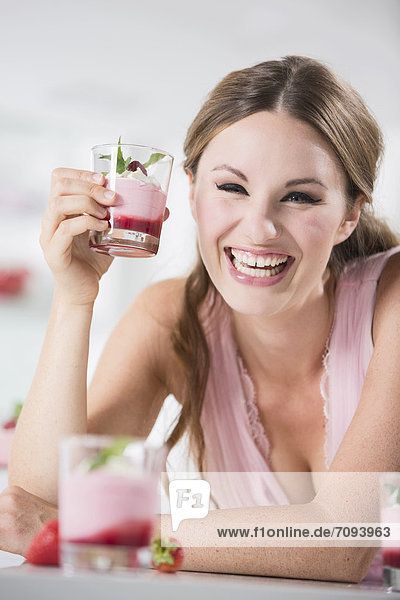 Deutschland  Junge Frau mit Joghurtglas  lächelnd  Portrait