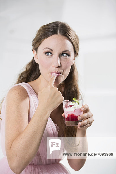 Deutschland  Junge Frau mit Glas Joghurt  Finger lecken