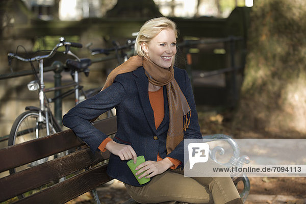 Europa  Deutschland  Nordrhein-Westfalen  Düsseldorf  Junge Frau mit Einwegbecher auf Parkbank  lachend