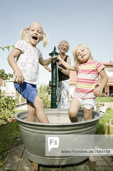 Deutschland  Bayern  Großmutter mit spielenden Kindern im Wasserbottich