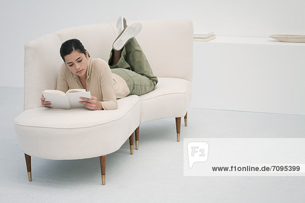 Young woman lying on chaise longue  reading book