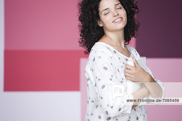 Young woman holding book to chest with eyes closed  smiling