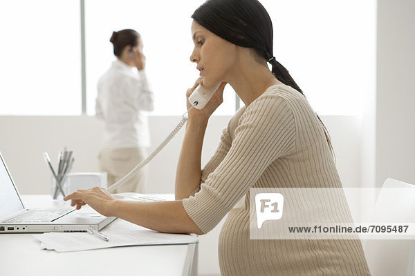 Young pregnant woman talking on landline phone in office  backlit