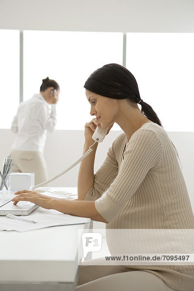 Junge schwangere Frau im Büro am Festnetztelefon  hintergrundbeleuchtet