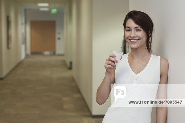 Young woman standing in corridor holding disposable cup