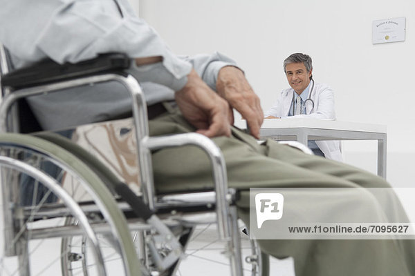 Doctor working in office  patient in wheelchair in foreground
