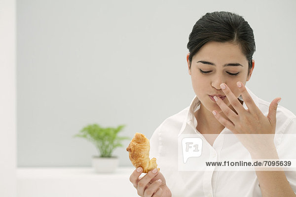 Junge Frau leckt Finger beim Croissantessen