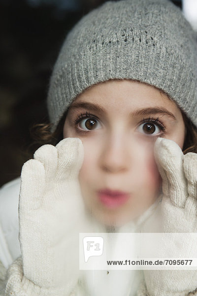 Girl breathing on window  dressed in winter clothes