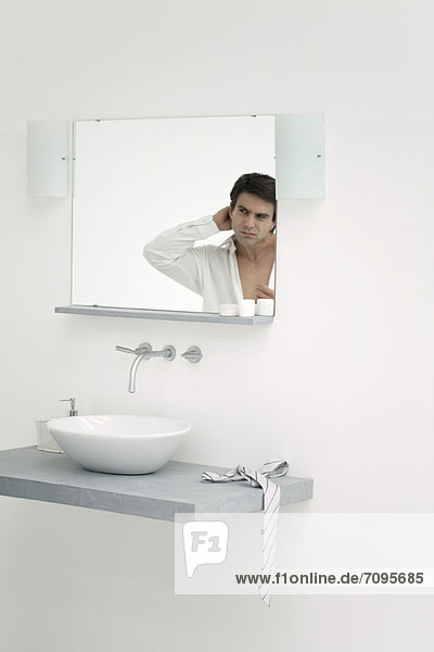 Mann schaut sich selbst im Badezimmerspiegel an