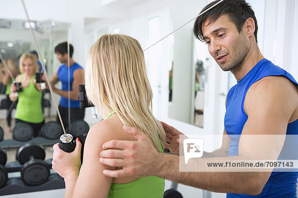 Trainer adjusting woman’s form in gym