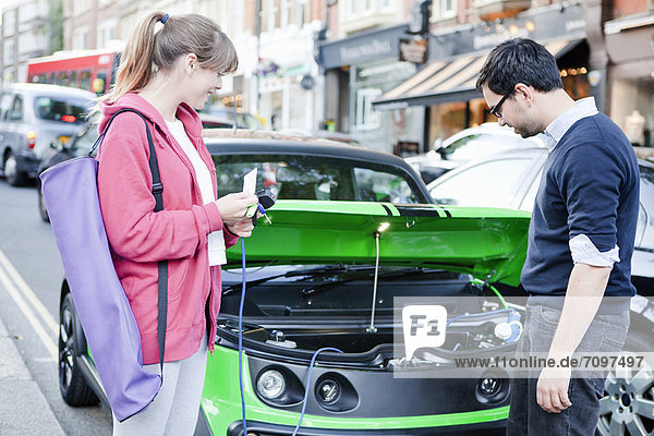 Couple charging electric car on street