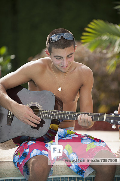 Teenager Junge spielt Gitarre am Pool