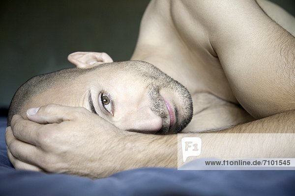 Barechested man with designer lying in bed