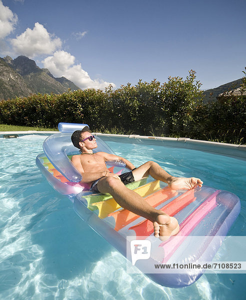 Man floating in swimming pool on inflatable raft
