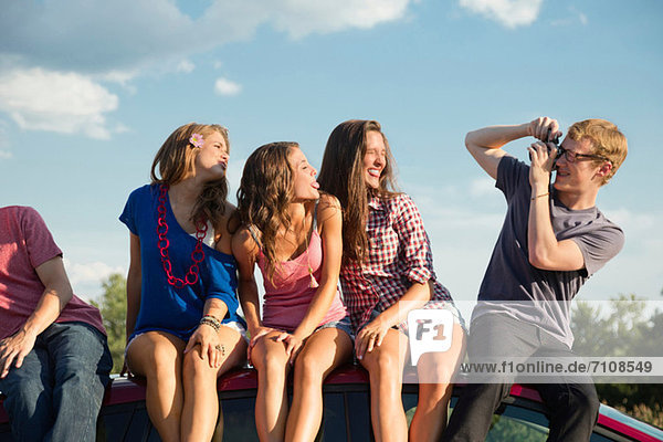 Freunde sitzen auf dem Autodach  junger Mann fotografiert
