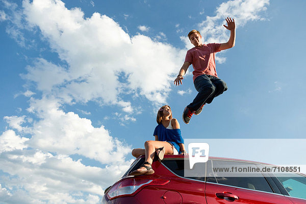 Junger Mann springt vom Autodach  Mädchen sitzt auf dem Dach