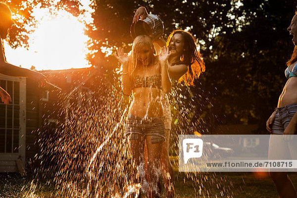 Mädchen gießt Eimer mit Wasser über den Kopf eines Freundes.