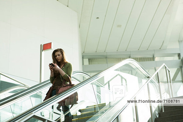 Junge Frau auf Rolltreppe mit Smartphone