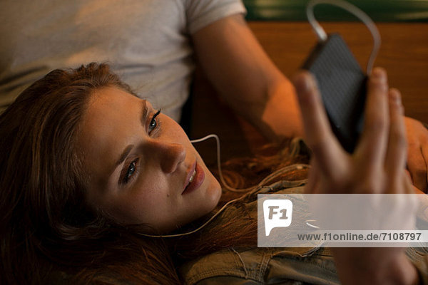 Young woman listening to music  lying on boyfriend's lap