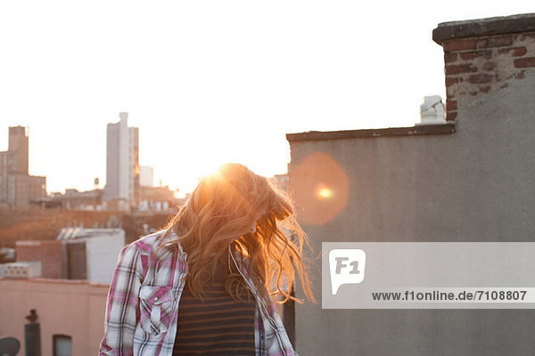 Junge Frau schüttelt Haare auf dem Stadtdach