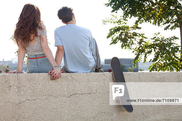 Young couple sitting on wall holding hands
