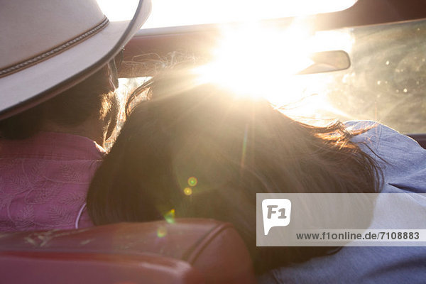 Woman resting head on boyfriend's shoulder as he drives in sunlight