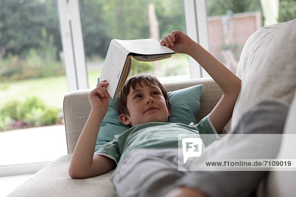 Junge liegt auf dem Sofa und liest ein Buch.