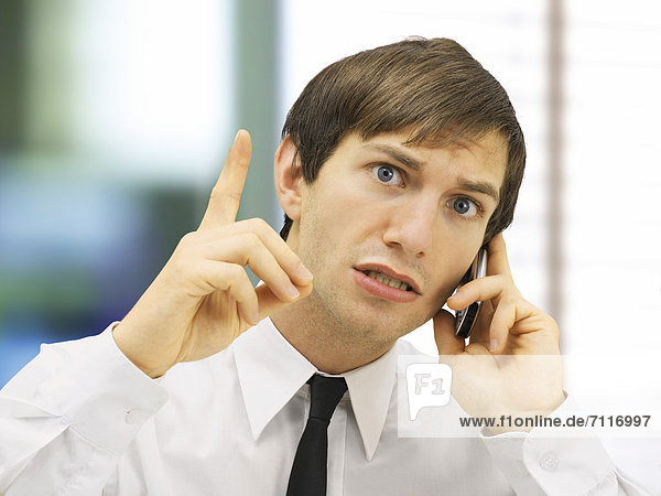 Stressed businessman speaking on his mobile phone  portrait  with an admonishing gesture  with a wagging finger