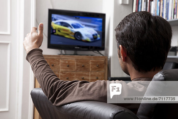 Man sitting on a leather sofa in front of a TV watching motorsport