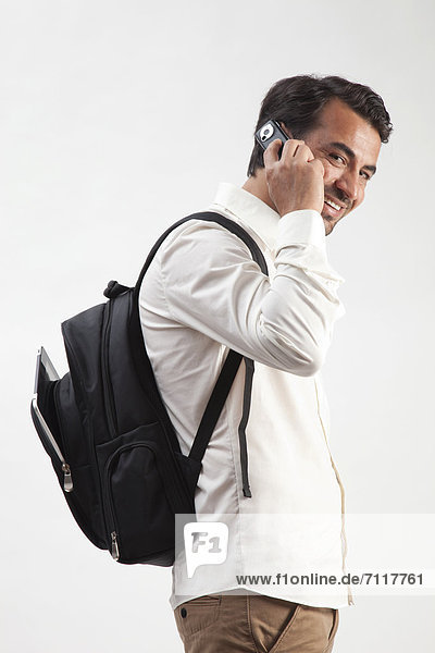 Man wearing a backpack  from which an iPad is sticking out  talking on a mobile phone