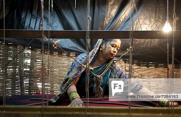 Woman in blue patterned sari weaving at loom in rough village shack  Naupatana weaving village  rural Orissa  India  Asia