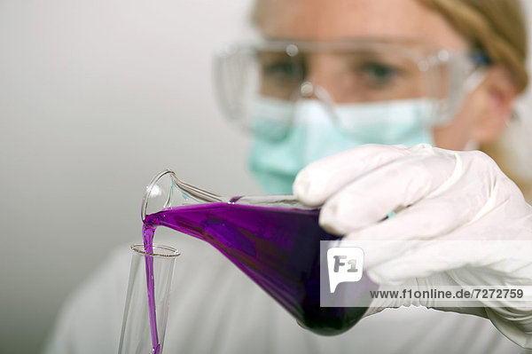 Chemikerin füllt Flüssigkeit aus einem Kolben in ein Reagenzglas