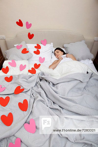 Frau schläft im Bett mit Herzformen auf der Bettwäsche
