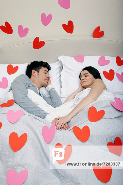 Paar im Bett mit Herzformen auf Bettwäsche