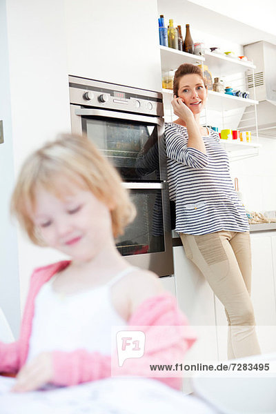 Mother on cell phone in kitchen with daughter in foreground