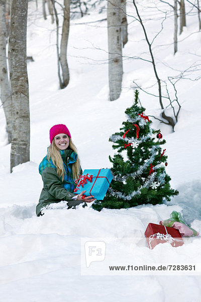 Woman sitting by christmas tree with gift