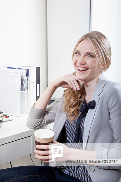 Glückliche junge Frau im Büro mit Kaffee
