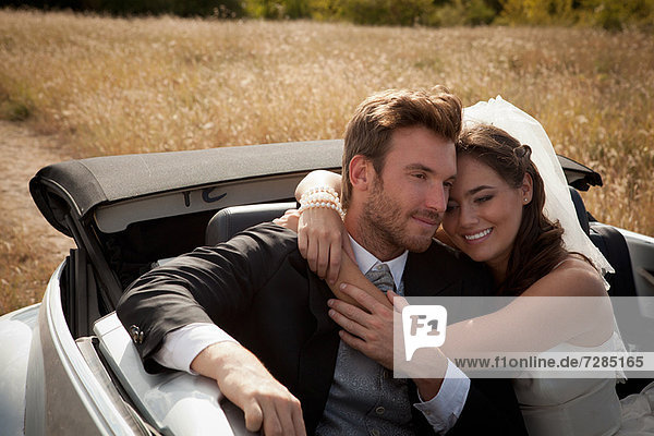 Newlywed couple hugging in convertible