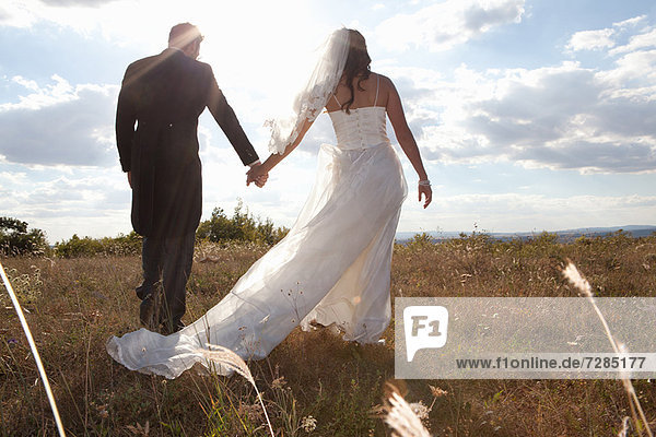 Newlywed couple holding hands in grass