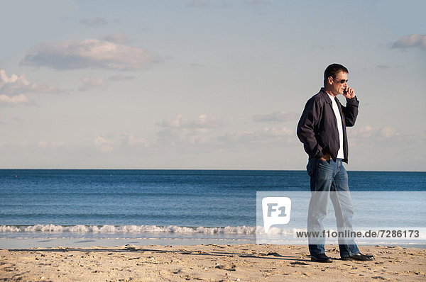 Mann  der am Strand mit dem Handy spricht.