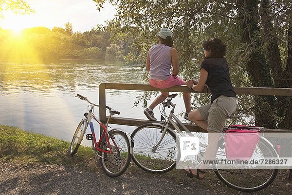 Women with bicycles relaxing by river