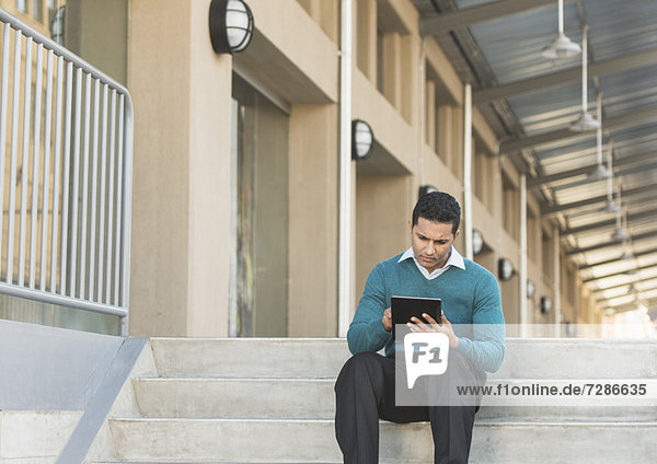 Man sitting on steps outside and using digital tablet