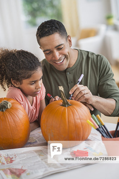Father and daughter (6-7) carving pumpkins for Halloween