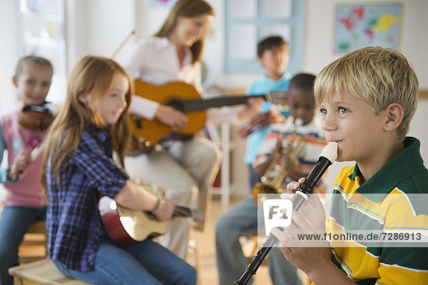 School children (8-9) with teacher playing instruments during music class